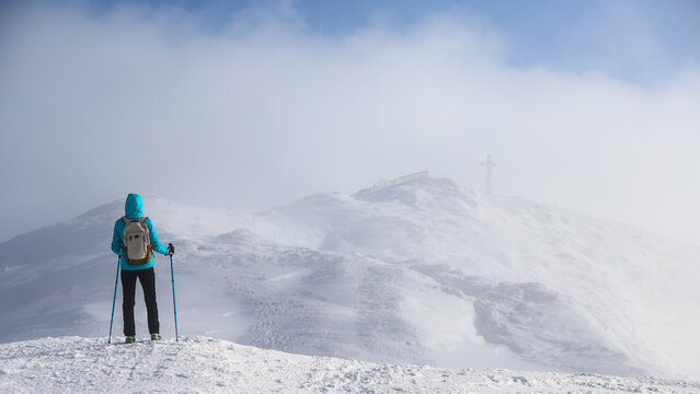 a girl hiker climbs a snowy mountainside with a mighty peak emerging from behind the clouds; the highest peak in the Polish Bieszczady mountains