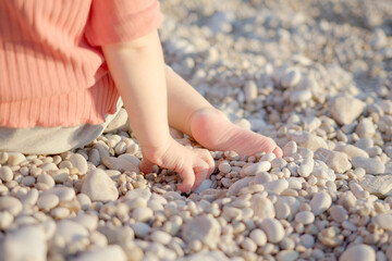 A cute child throws pebbles and has fun. Little girl is playing on the seashore. Rest on the sunset sea