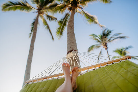Close-up of feet in hammock, palm trees in background, vacation concept.