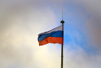 Flag of Russia in stormy sky with dark clouds on high flagpole.