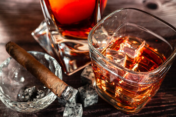 A glass of scotch whiskey with ice and a cigar on a wooden table close-up.