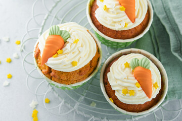 Carrot cake cupcakes for Easter. Carrot cupcakes with cream cheese frosting decorated with tiny marzipan carrots on white background. Happy Easter and spring holiday concept. Holydays homemade dessert