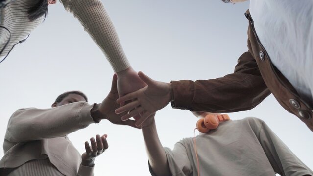 Low angle of unrecognizable friends in casual clothes stacking hands together against cloudless blue sky