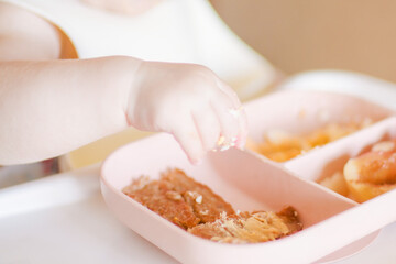 A Little baby eating her dinner and making a mess. Top view of little kid holding food in his...