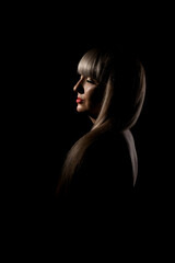 Beautiful girl with blond bangs fringe against black background. Abstract sidelit portrait. .