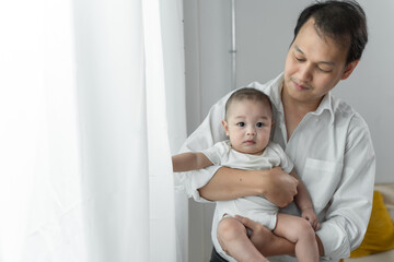 Asian young father working from home while holding his baby boy and smiling while making a break from his work.