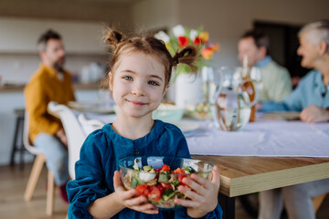 Little girl holding bowl with salad, preparations for family dinner.