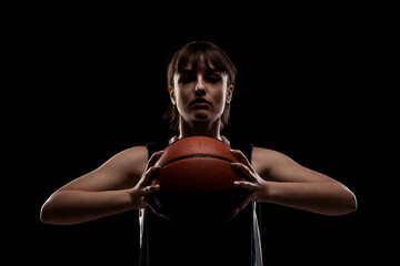 Female basketball player. Beautiful girl holding ball. Side lit half silhouette studio portrait against black background. - Powered by Adobe