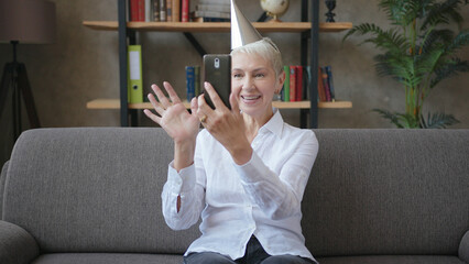 Happy business elderly woman in birthday cap talking on video call using smartphone