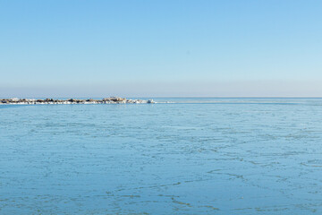 Close-up of the icy seashore, frozen waves, rocks and sun glare on the ice