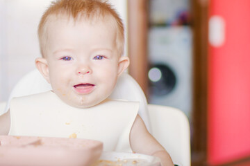 Happy childhood and delicious food. Grimaces of a cheery baby. Close-up of a child's face. Little cute kid eats with his hands. Funny child gets dirty with food
