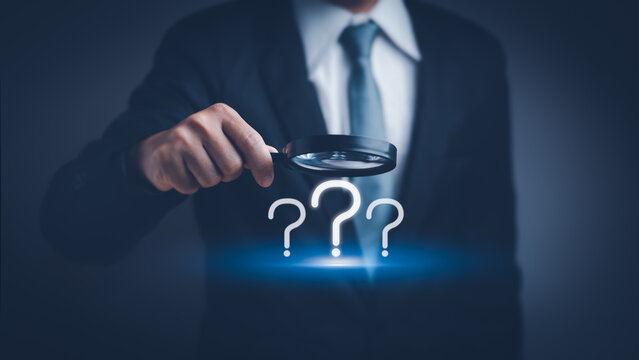 businessman hand holding a magnifying glass with question mark icon , concept of analyzing problem Or find the cause that occurs during the work process