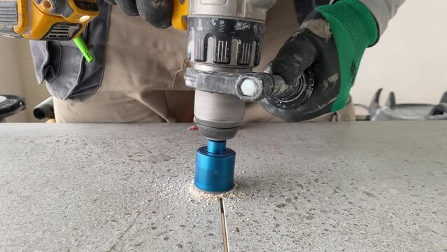 Worker tiller drills round hole in porcelain tile with a diamond core.
