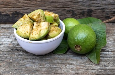 Guava Pieces Coated with Salt, Chili Powder and Spices in a White Bowl with Whole Guava Fruit Isolated on Wooden Background