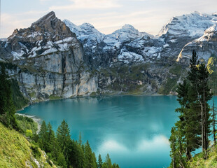 Idyllic morning view of the lake Oeschinensee. Location Swiss alps, Switzerland, Kandersteg district. Blue mountain lake with pine trees and mountains in background.