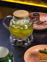 green tea in a transparent teapot with apple and lime with cake