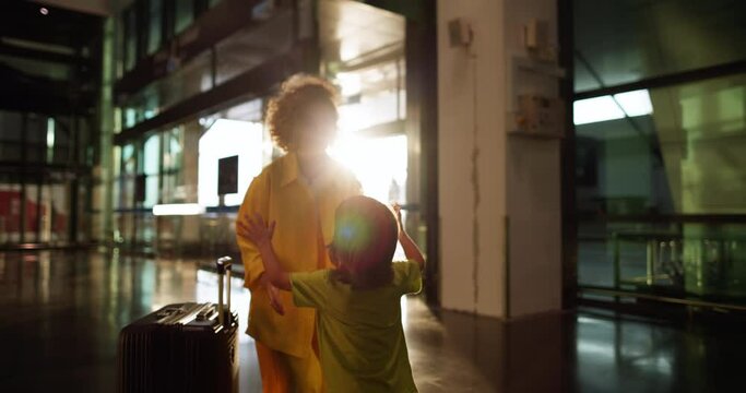 Child in rays of setting sun runs to his mother at airport. Woman returned from vacation and finally met her beloved son. The joy of long-awaited meeting with loved one. Strong hugs of mother and son
