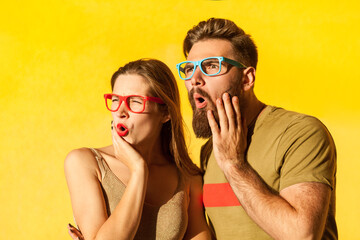 Amazed couple in glasses looking away with astonished facial expression, being shocked and surprised