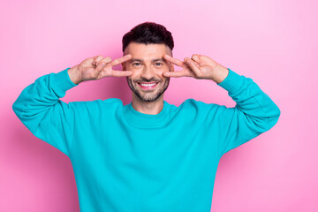 Photo of good mood positive guy student wear blue sweater showing v-sign cover fingers face peaceful candid person isolated on pink color background