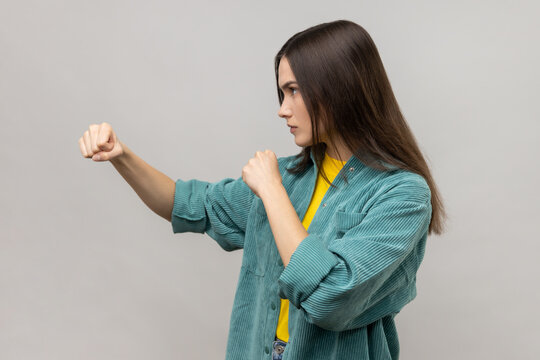 Side view of woman standing with clenched fists, furious look, ready to punch, expressing aggression