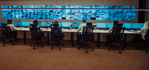 Group of Security data center operators working in a CCTV monitoring room looking on multiple monitors.Officers Monitoring Multiple Screens for Suspicious Activities