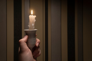 Human in a dark room holds a light bulb holder in his hand with a burning candle inside (close-up)....