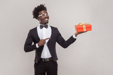 Happy positive man in glasses standing pointing at red present box, gift for holiday.