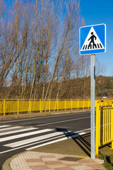 Paso de peatones con señal a la entrada de un puente con barandillas amarillas