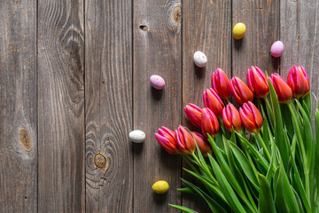 Easter background with a bouquet of pink tulips and Easter eggs on a wooden background, top view, copy space.