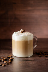 Glass cup of layered coffee drink with milk foam, coffee beans over wooden background, copy space