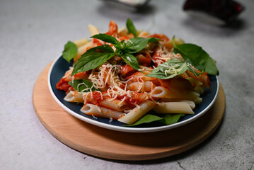 pasta in tomato sauce with basil leaf on a plate on a wooden tray