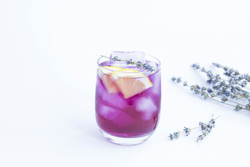 Lavender lemonade with ice and lemon in the drinking glass on the white background. Close-up. Copy space.