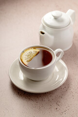 Drinking tea, white ceramic cup and tea pot with black tea and lemon slice.