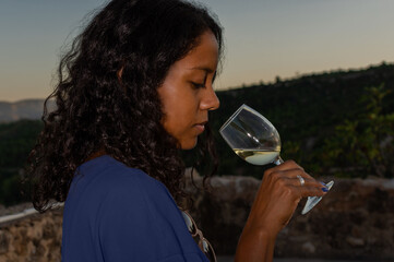Young brunette woman with curly hair holding a glass of white wine outdoors