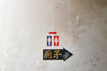 Vintage rustic dirty wall with man an female toilet sign and a Chinese wording with black arrow pointing to the toilet direction