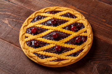 Cherry shortcrust pastry pie decorated with cherries and pastry grill on a wooden table.