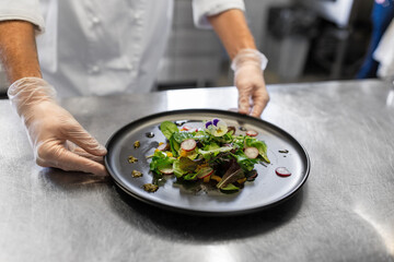 food cooking, profession and people concept - close up of male chef cook with plate of salad at restaurant kitchen table