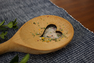 wooden spoon with a heart cut-out lies diagonally on a blue and white doily on a dark wooden table...