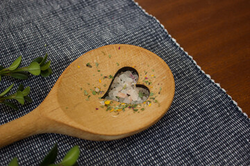 wooden spoon with a heart cut-out lies diagonally on a blue and white doily on a dark wooden table...