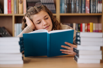 Attractive happy young girl student studying at the college library, sitting at the desk