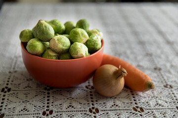 Brussels sprouts in a clay pot, next to onions and carrots, healthy vegetables.