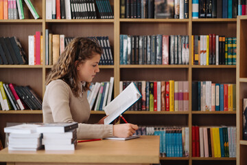 Attractive happy young girl student studying at the college library, sitting at the desk