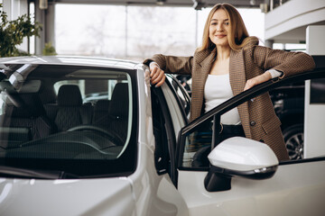 Young woman standing by new car in car showroom