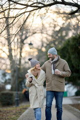 Fototapeta premium A happy romantic couple with coffee walking outdoors in the park
