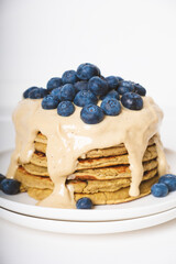 Delicious freshly cooked thick and fluffy protein pancakes stacked on white plate, served with cashew cream and fresh blueberries. Healthy food, low carb diet.