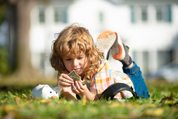 Fototapeta na wymiar Piggy bank for money. Kid saving money for purchase, hold pink piggy bank, laying on grass. Child learning to calculate personal budget, manage finance, playing investment, accounting.