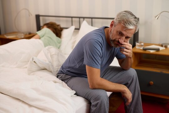 Mature man looking worried while his wife sleeps in the background