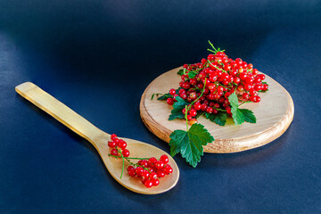 Red currants in a glass. On a wooden background, a light green napkin with leaves and red berries, on a napkin a glass transparent glass with red currant berries. 