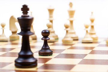 moving black pawn and queen against white chess pieces in background on wooden chessboard close up (focus on the black pawn)