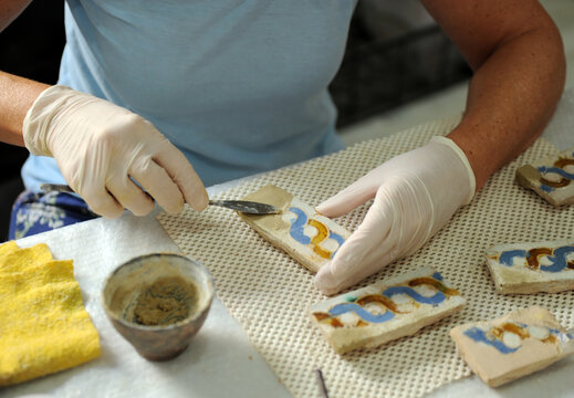Close up of the hands of a restorer of artistic and cultural heritage restoring old tiles in the restoration workshop